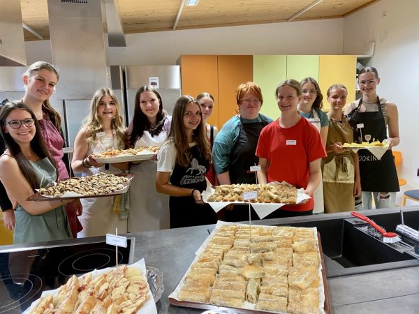 Die Schülerinnen und Schüler stehen vor einem Tisch mit Gebäck und zeigen ihre fertigen Backwaren