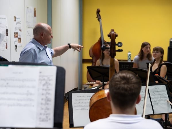 Blick von hinten in das Orchester, die offenen Partituren und Streichinstrumente sind zu sehen